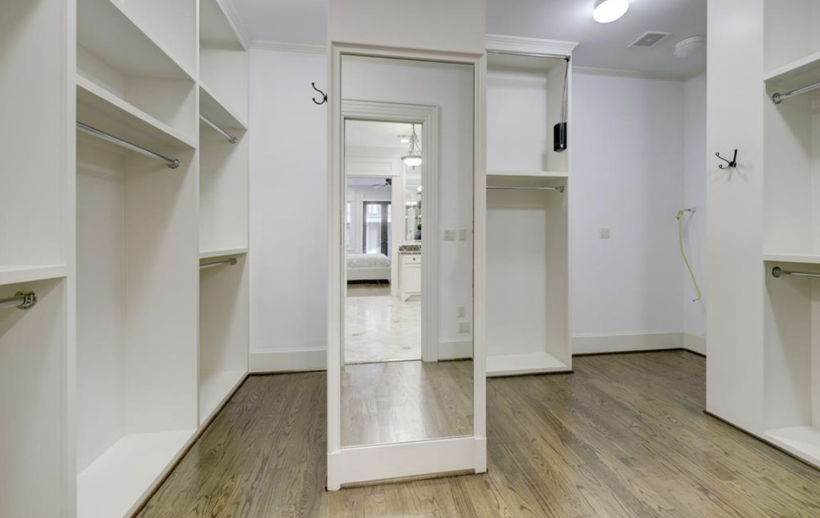A massive walk-in closet with a white interior, wooden floors, and a mirror located in the center of the room.